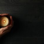 Candle in female hands on wooden background, space for text