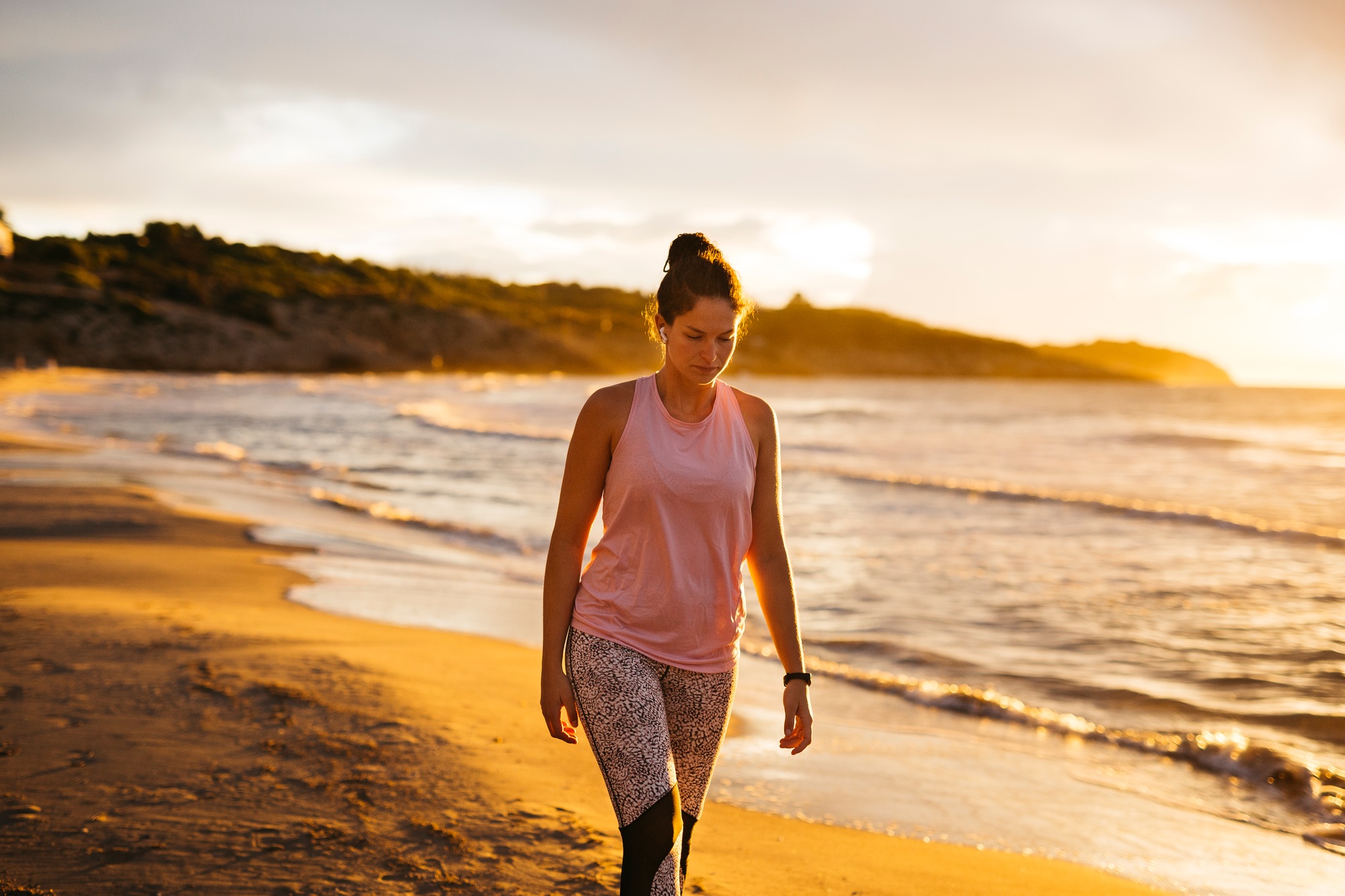 Young sportswoman walking on the beach at sunset after exercising