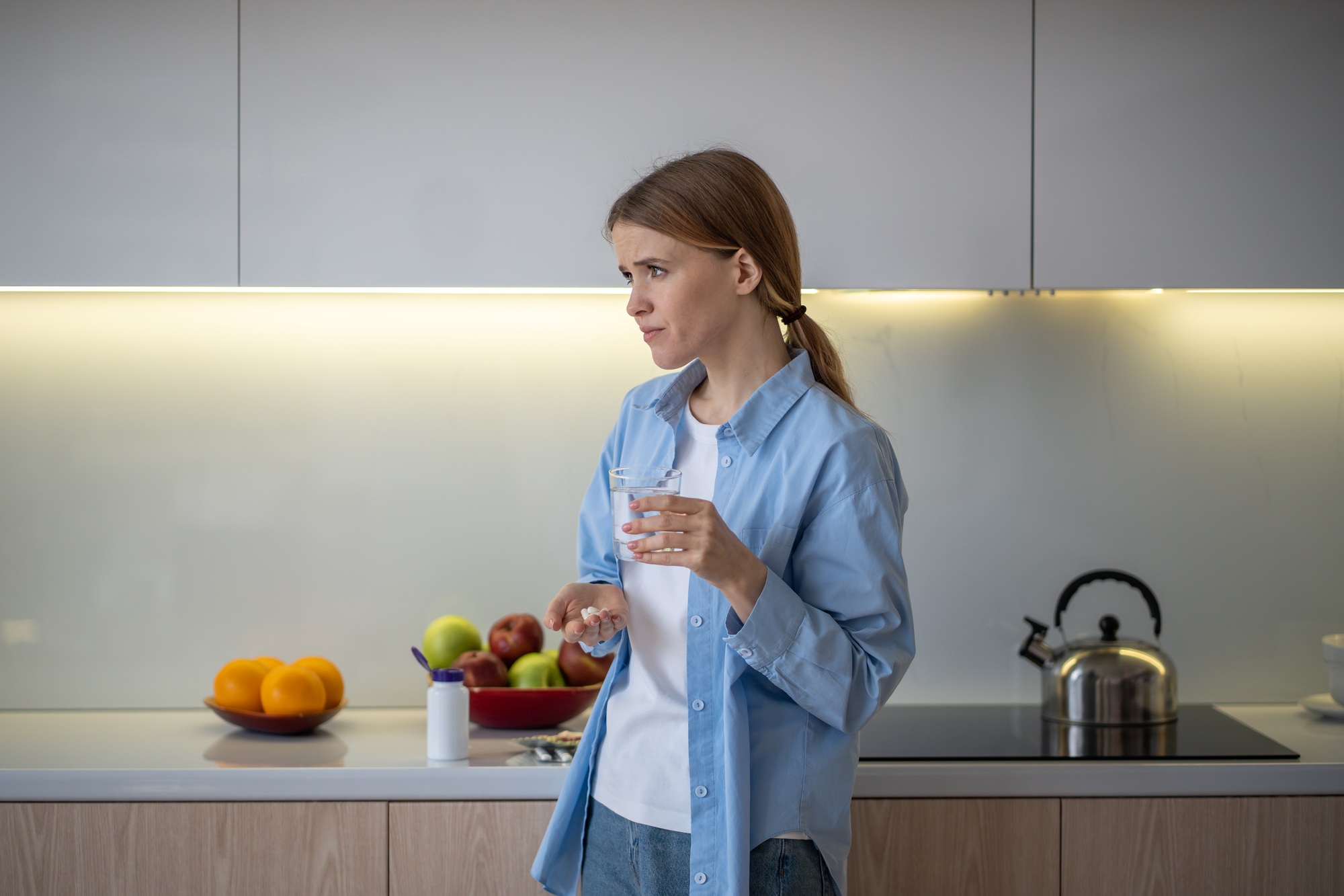 Woman taking medication vitamins dietary supplements standing on kitchen at home.